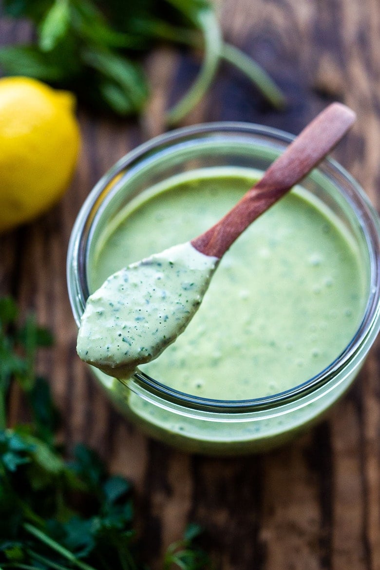 Green Tahini Sauce with a wood spoon in a jar.