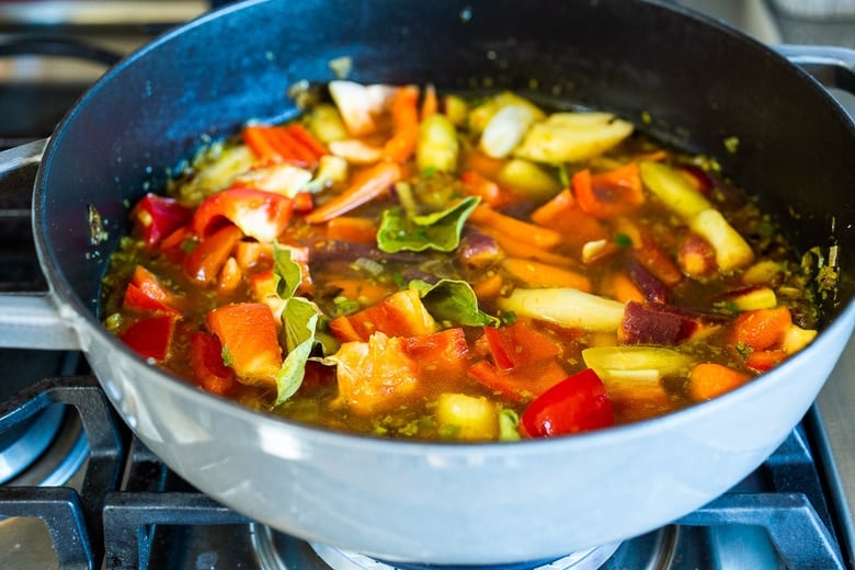 chopped veggies in broth in pan with kaffir lime leaves.