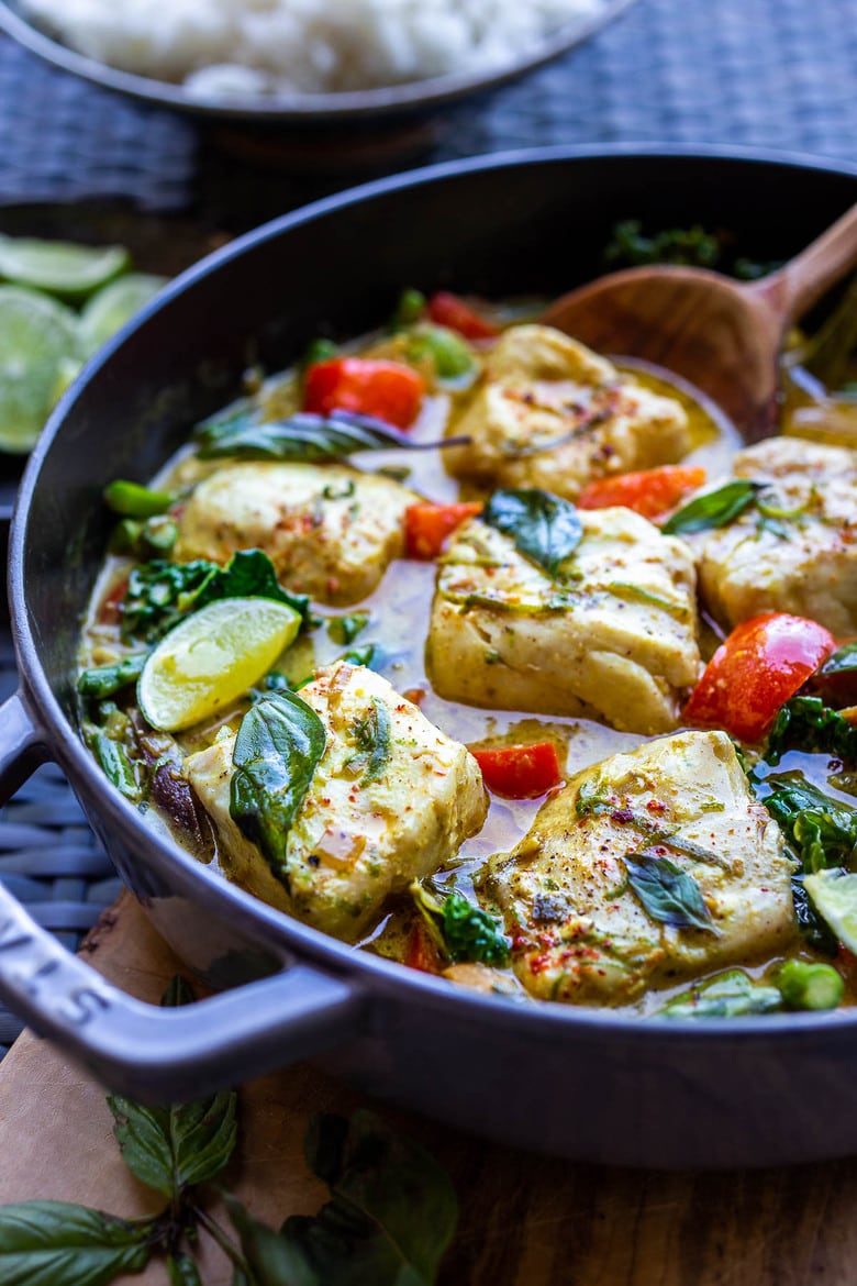pot of thai fish curry seasoned with basil and lime wedges.