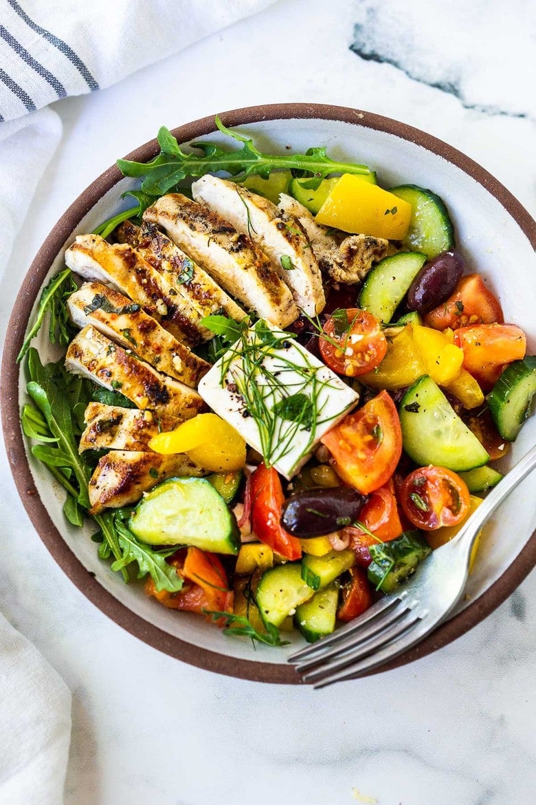 Grilled chicken Greek salad with sliced grilled chicken, chopped cucumbers, tomatoes, peppers, and olives, served with arugula, dill, and feta.