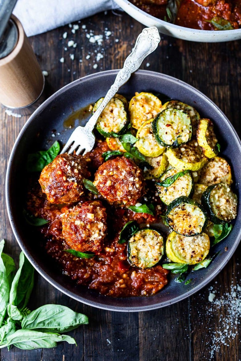 bowl with baked zucchini with pecorino and meatballs with marinara and fork.