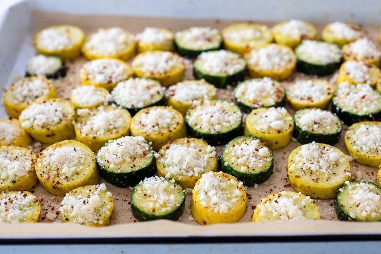 zucchini and yellow squash disks with pecorino cheese on parchment-lined baking sheet.