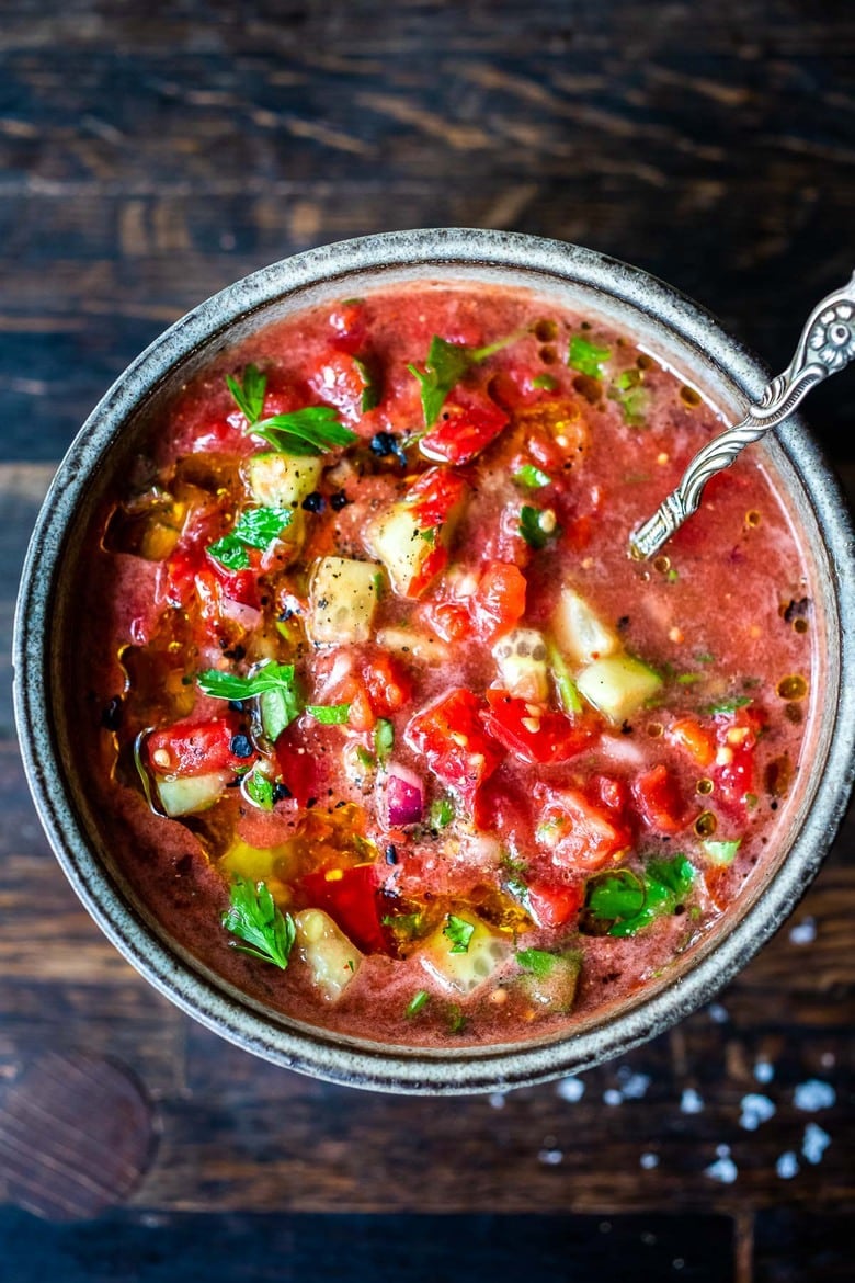 chunky tomato gazpacho topped with fresh tomato and cucumber and fresh basil, in bowl with spoon.