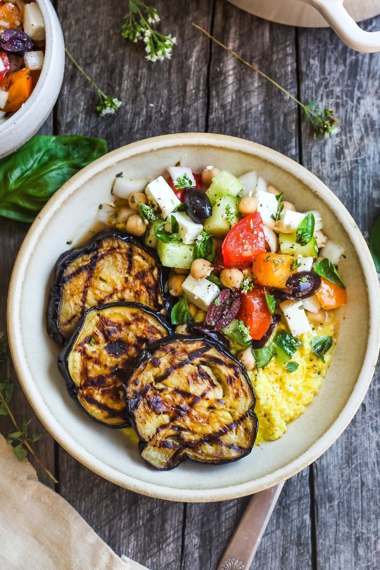 grilled eggplant with Greek relish and creamy polenta in ceramic bowl, garnished with fresh basil.