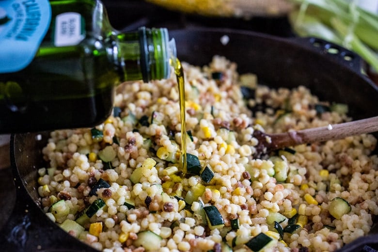 pouring olive oil into skillet of fregola sarda with zucchini and corn.