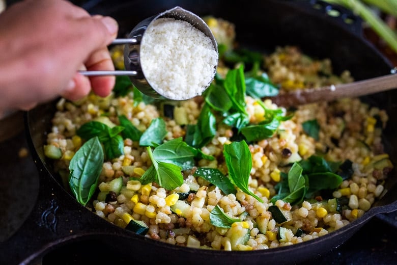 adding pecorino and basil leaves to the fregola sarda.