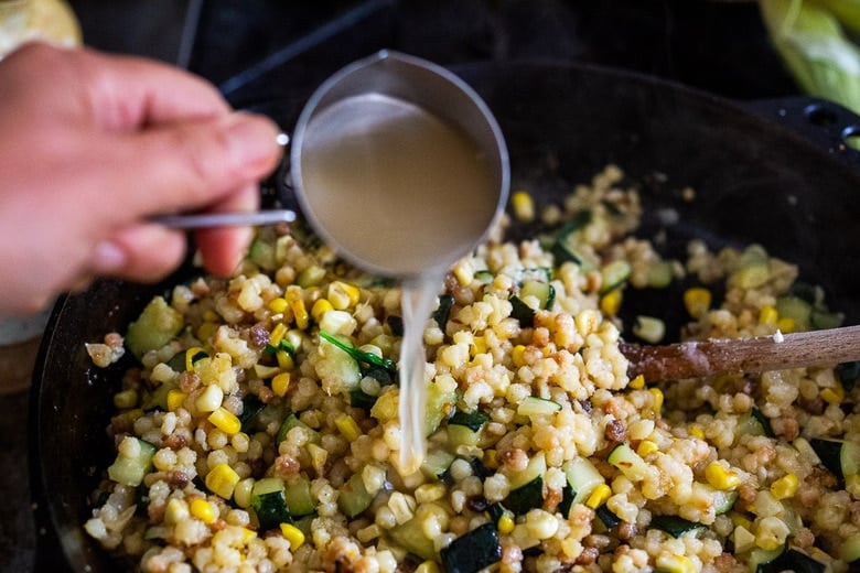 adding pasta water to the pan of fregola sarda.