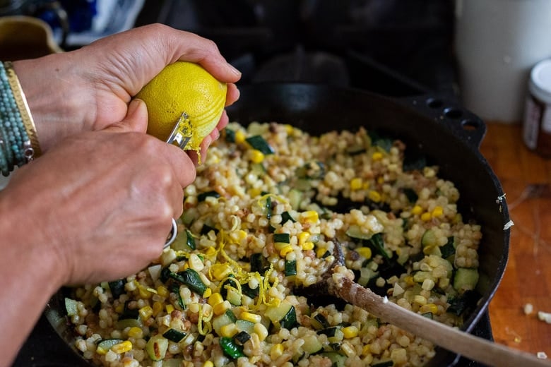 hands zesting a lemon to add lemon zest to the pan with fregola sarda.
