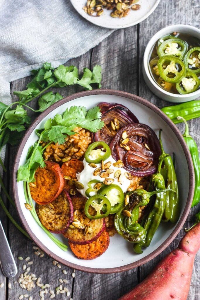 bowl with Mexican rice, roasted yams, red onions, shishito peppers, pickled jalapeños, pumpkin seeds, and sour cream.