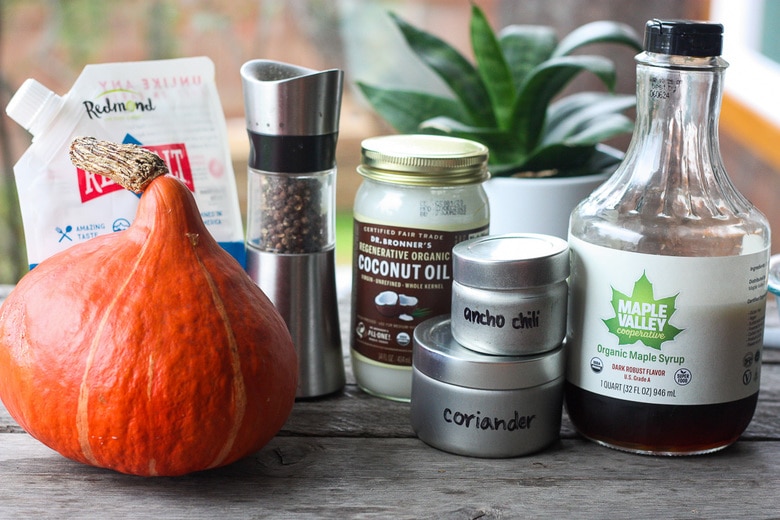 ingredients for roasted red kuri squash on wood table - red kuri squash, salt, pepper, coconut oil, ancho chili, coriander, maple syrup.
