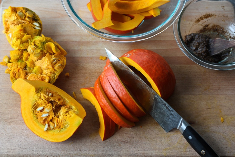 sharp knife cutting strips of red kuri squash on wood cutting board.