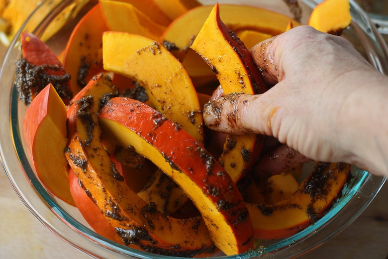 hand rubbing spice mix on the red kuri squash slices in glass bowl.