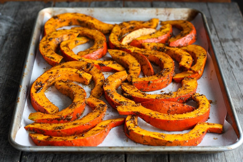 seasoned red kuri squash slices on parchment lined baking sheet.