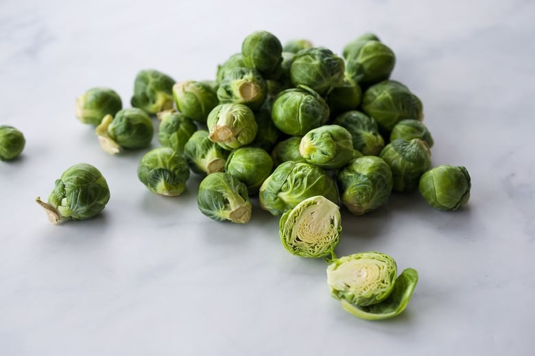 a Brussels sprout cut in half on a surface in front of a pile of whole Brussels sprouts.