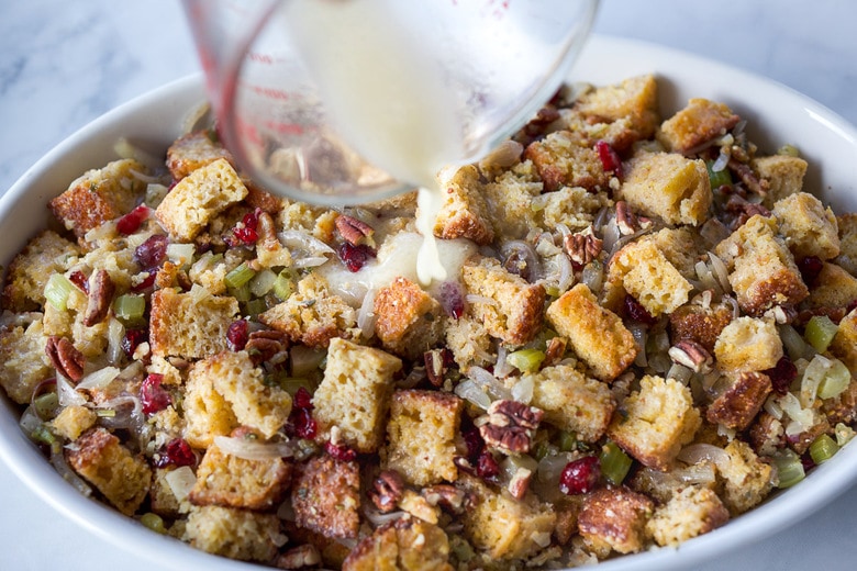 pouring broth over stuffing in baking dish.