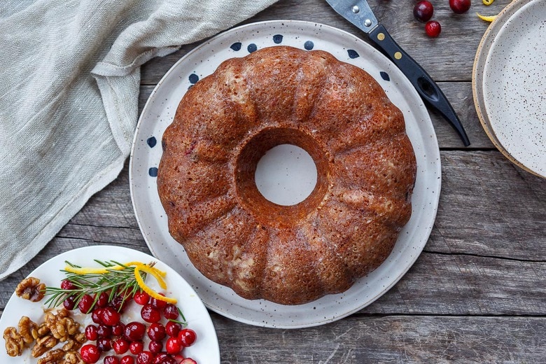 baked bundt cranberry cake on plate next to plate of toppings.