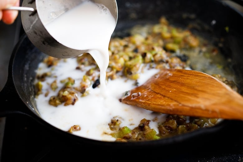 pouring cup of almond milk into skillet with sautéed celery and onion.