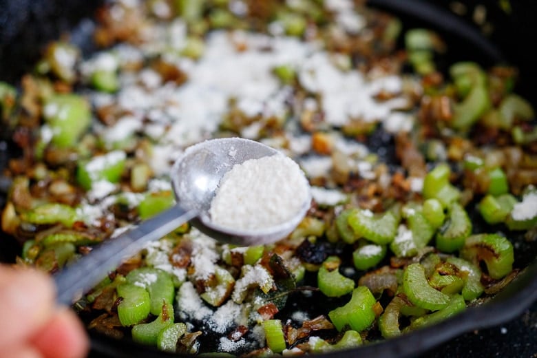 teaspoon of flour held over the cast iron skillet with sautéed celery and onion.