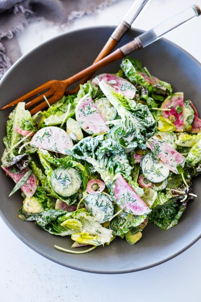 salad bowl and serving utensils with little gem salad tossed in dilly ranch dressing.