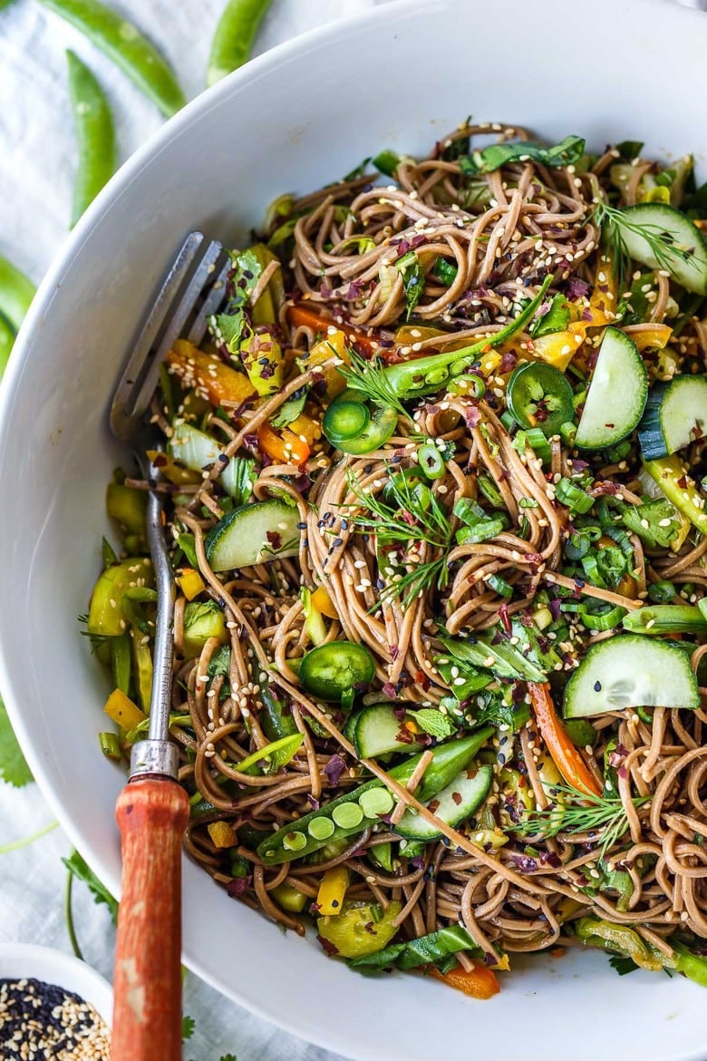 soba noodle salad with raw veggies, garnished with fresh herbs and sesame seeds.