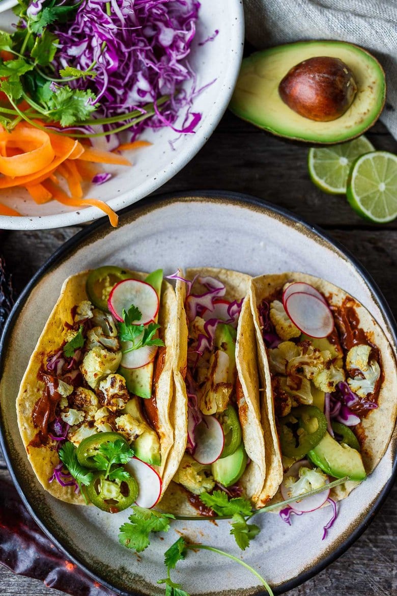 Roasted Cauliflower Tacos with quick and easy Mole Rojo sauce! These healthy vegan tacos are loaded up with cabbage, avocado, radishes and cilantro and full of satisfying flavor and fresh crunchy ingredients.