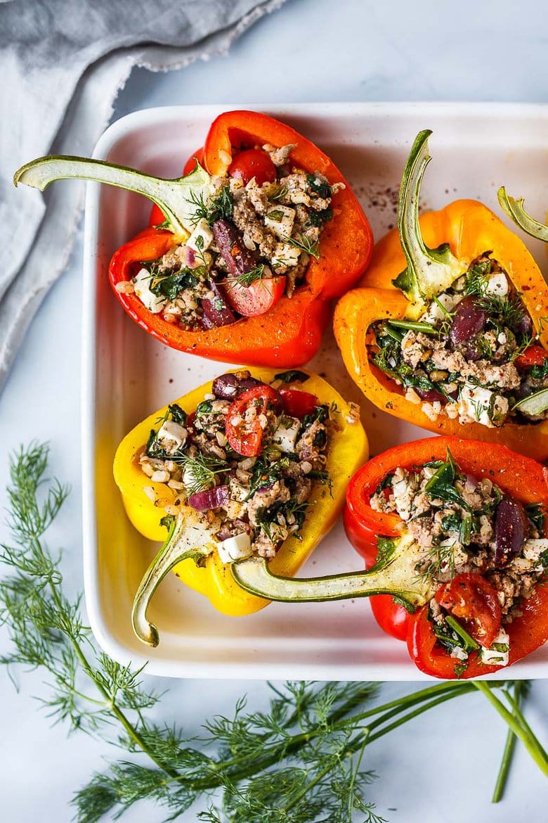 Mediterranean stuffed peppers with rice, ground turkey, olives, tomatoes, feta, and fresh dill in baking tray.