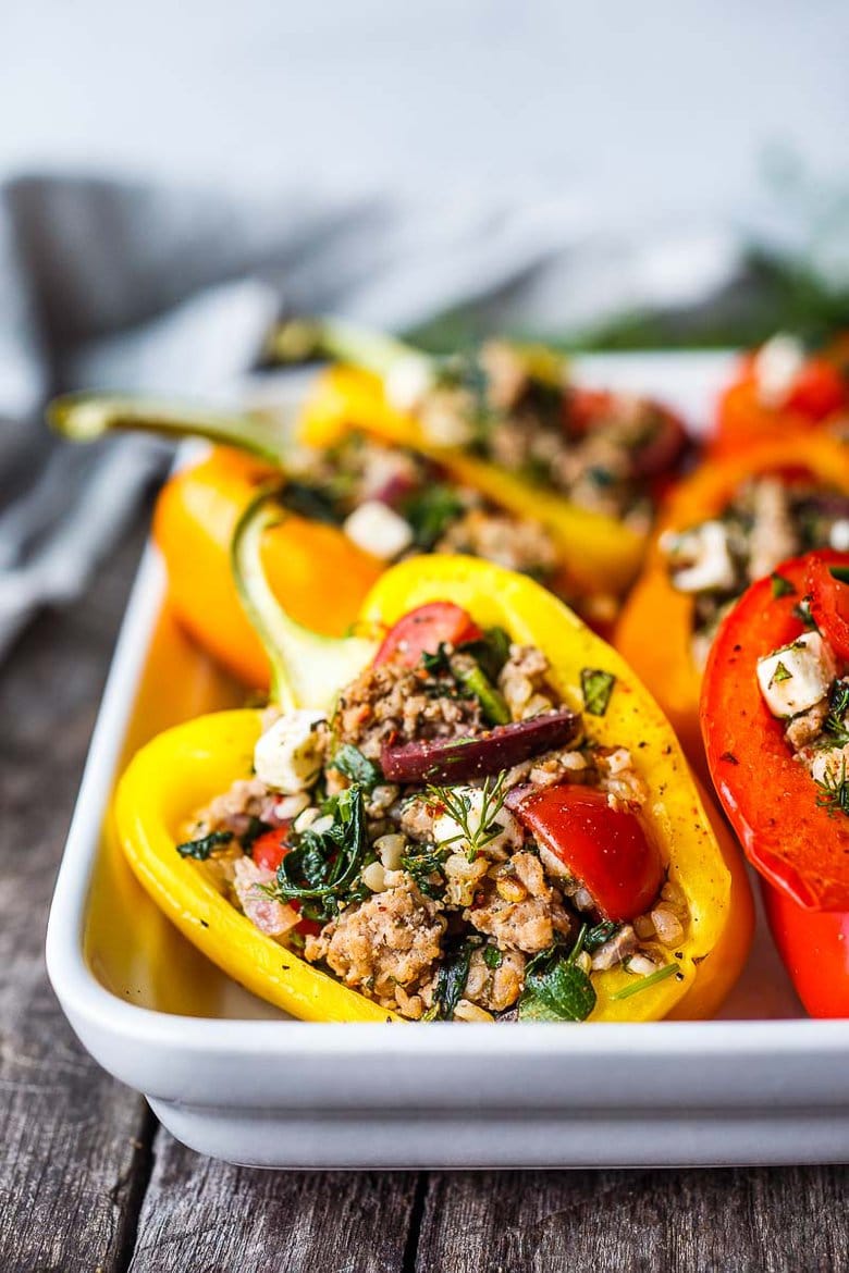 a Mediterranean stuffed bell pepper on a baking tray, filling with rice, ground turkey, tomatoes, olives, herbs, feta, and spinach.