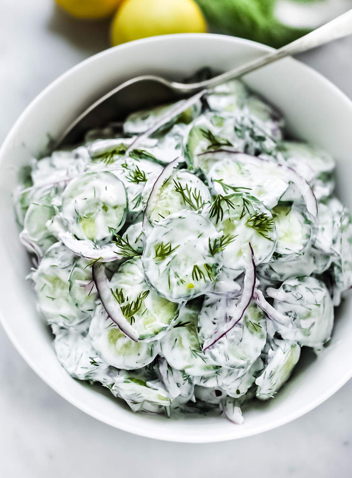 Creamy Cucumber Salad in a white bowl with cream yogurt dill dressing.