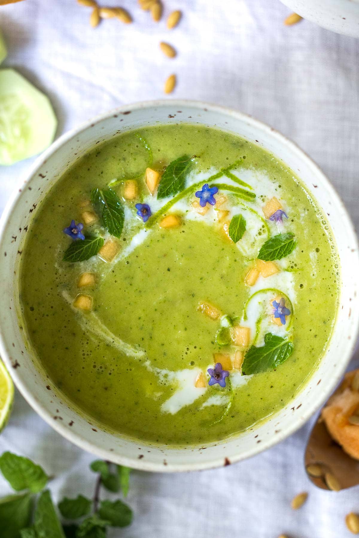 Cucumber Melon Soup in a pottery bowl swirled with cream, flowers and herbs