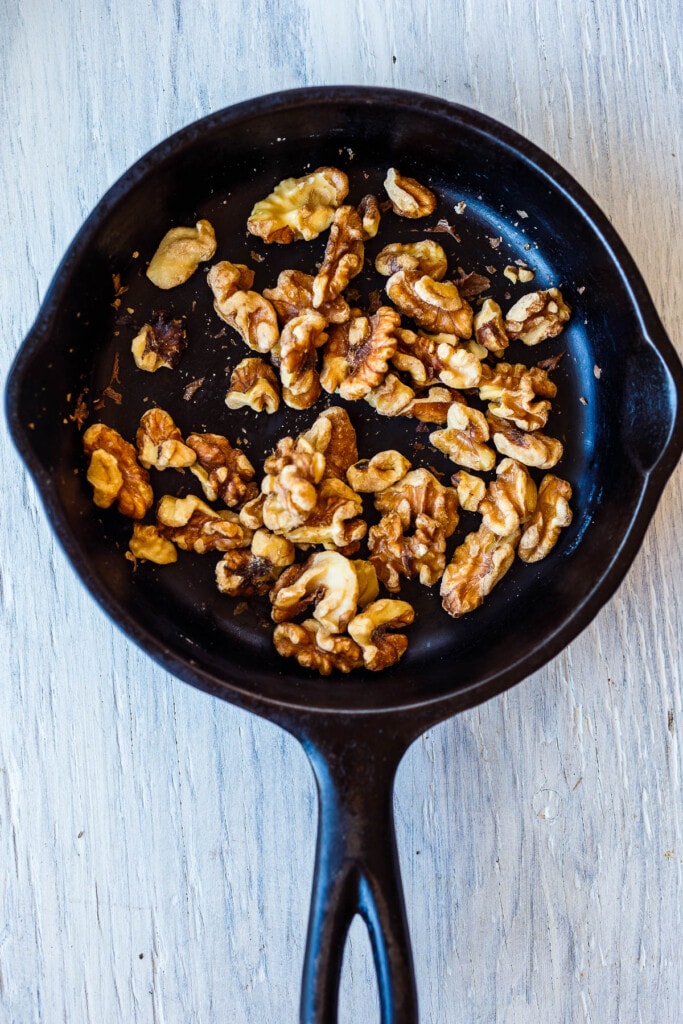 Walnuts toasted in a small round cast iron skillet.