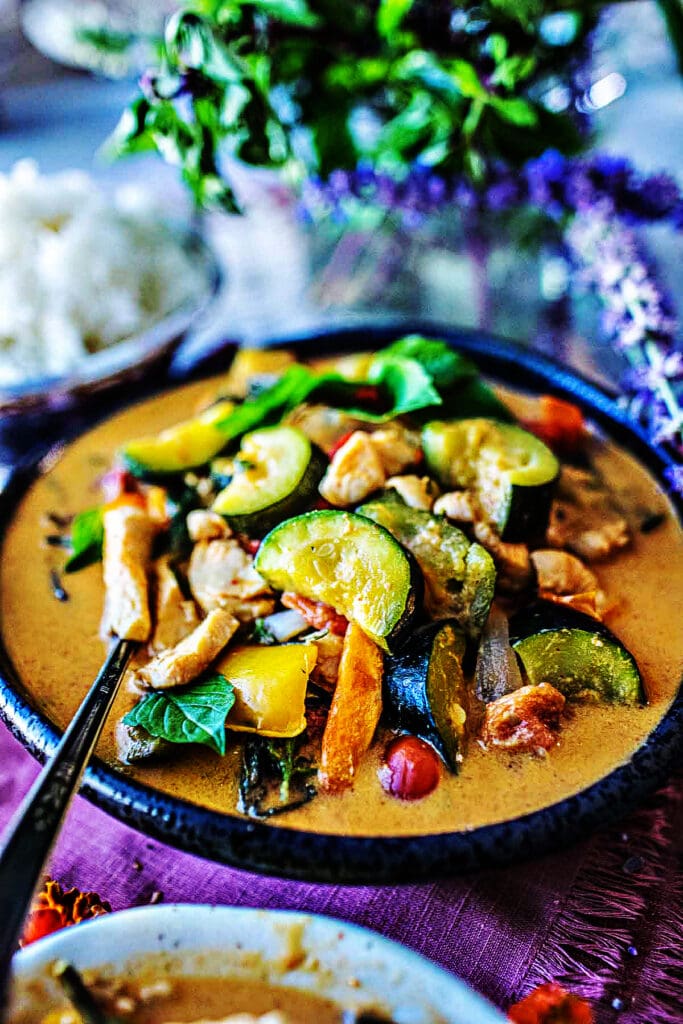 bowl of zucchini curry in coconut milk sauce with colorful veggies and chicken breast.