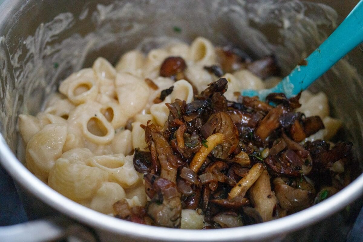 Adding half of the sautéed mushrooms to the Mac and cheese.