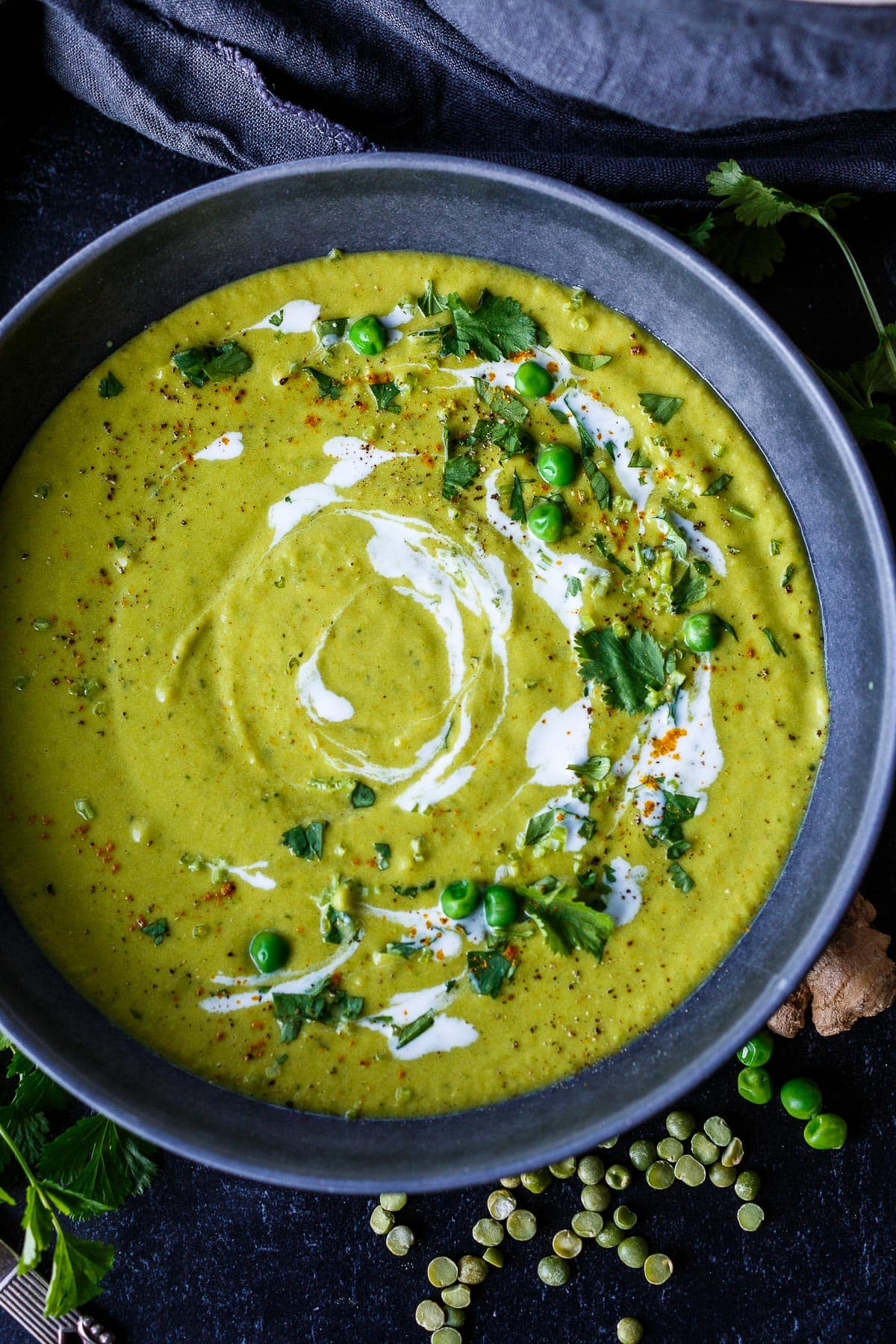 bowl of curried split pea soup, garnished with drizzle of coconut milk, fresh peas, fresh herbs, and spices. 