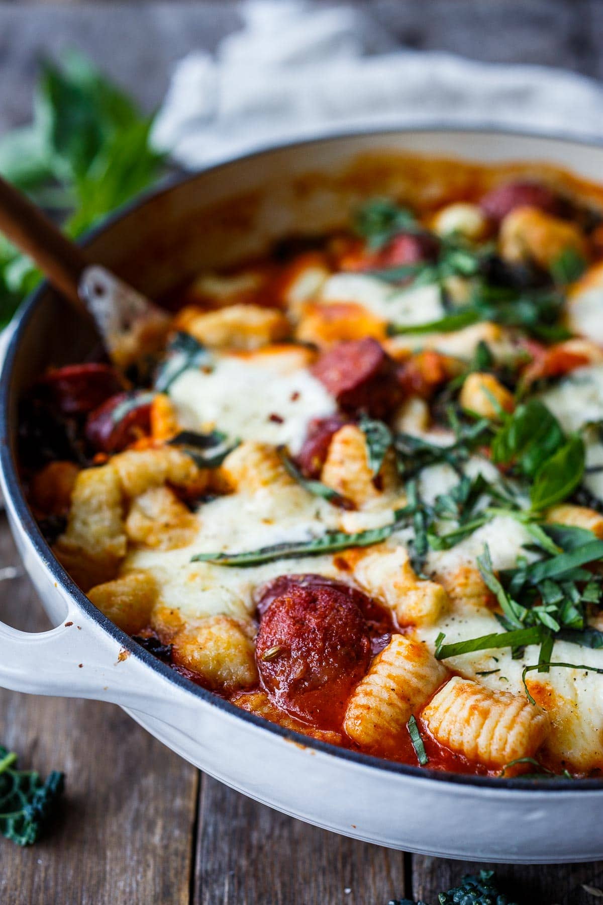 Baked gnocchi with tomato sauce, kale sausage and cheese served on a plate.