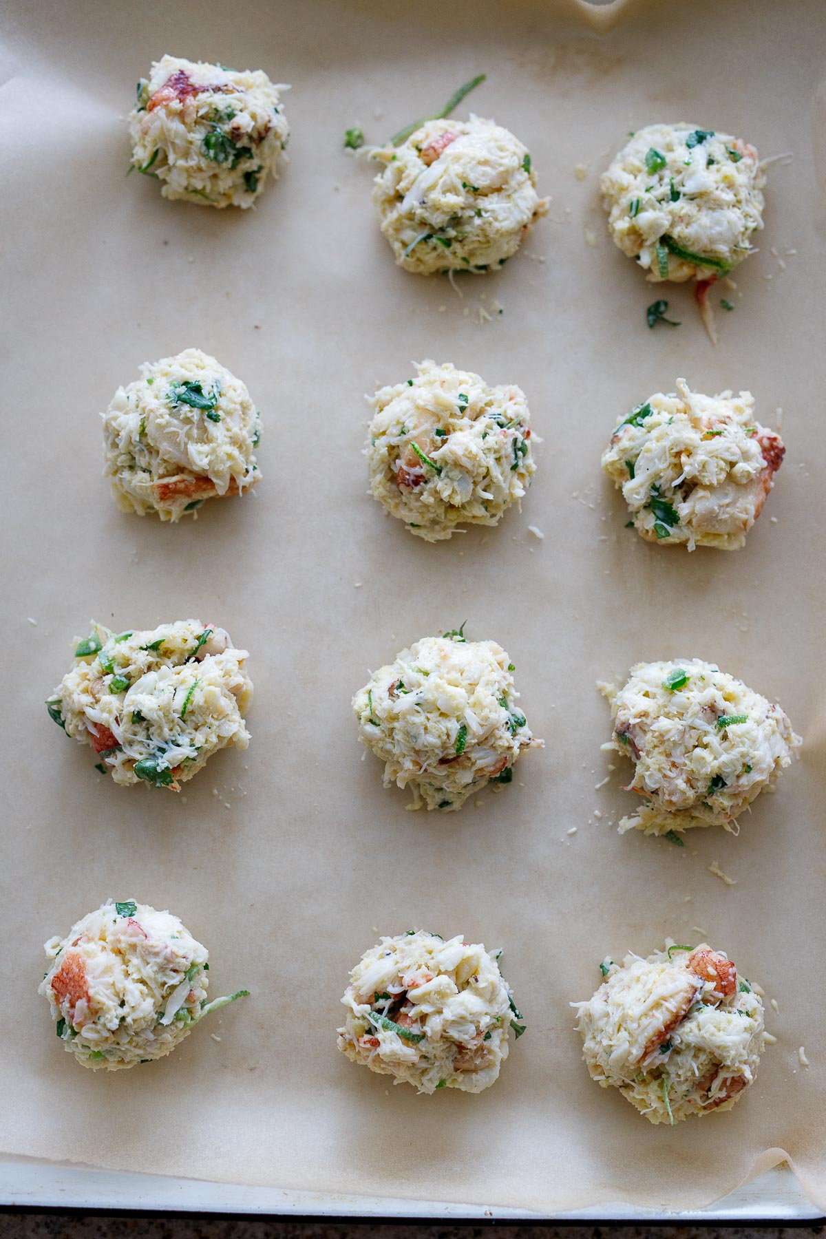 Twelve hand-formed crab cakes on a sheet pan. 