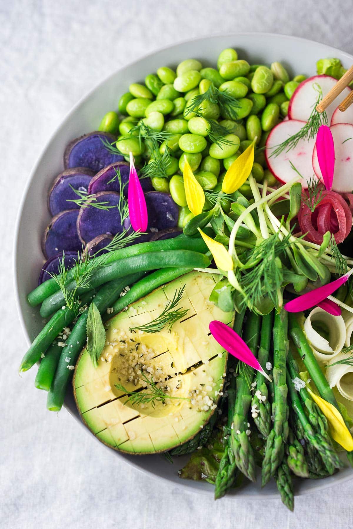 This Green Goddess Bowl features asparagus, green beans, avocado, edamame, purple potatoes and a vegan green goddess dressing. 