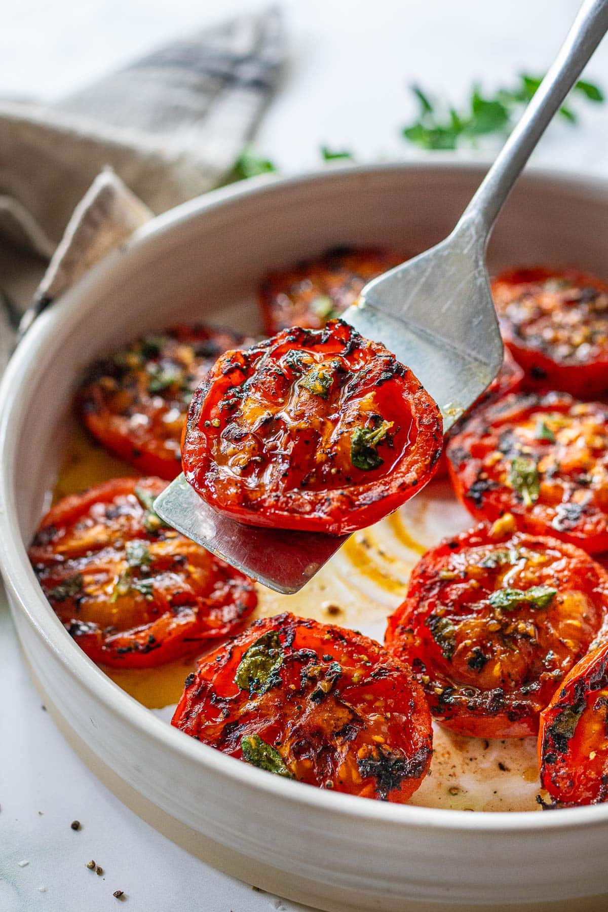 Savory grilled tomatoes with garlic and oregano, olive oil, and balsamic vinegar. In a serving bowl, being served.