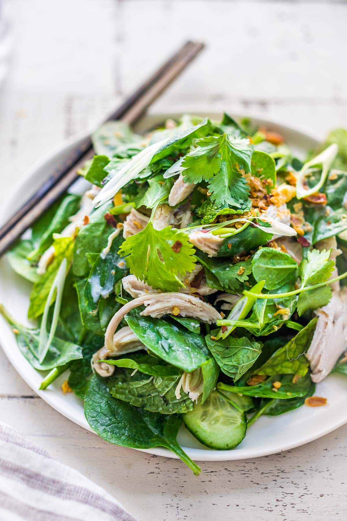 A spinach salad with coconut poached chicken, crunchy veggies, and herbs.