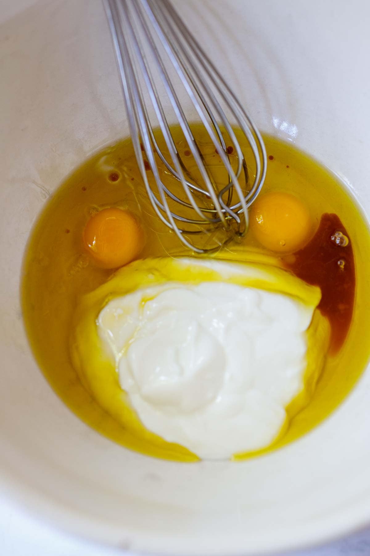 mixing the eggs, vanilla, yogurt and oil with a whisk in a white bowl.