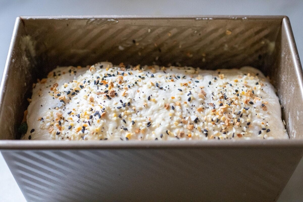 unbaked jalapeno cheddar sourdough in loaf pan with everything bagel seasoning on top.