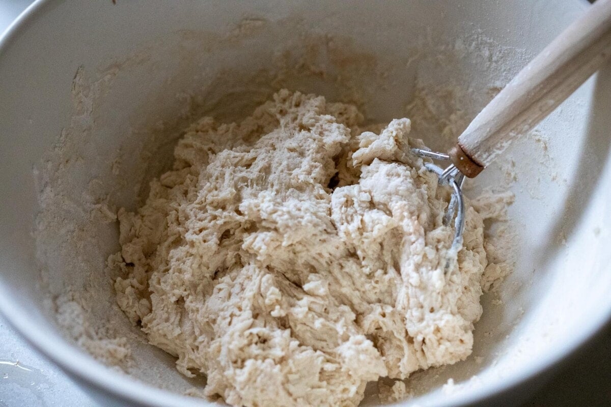 large mixing bowl with bread dough and dough whisk.