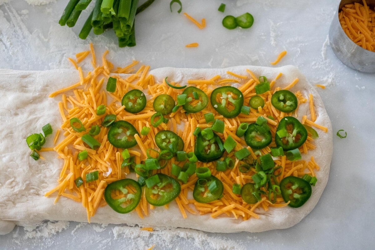 dough spread into rectangle shape with right half topped with shredded cheddar cheese, jalapenos, and scallions.