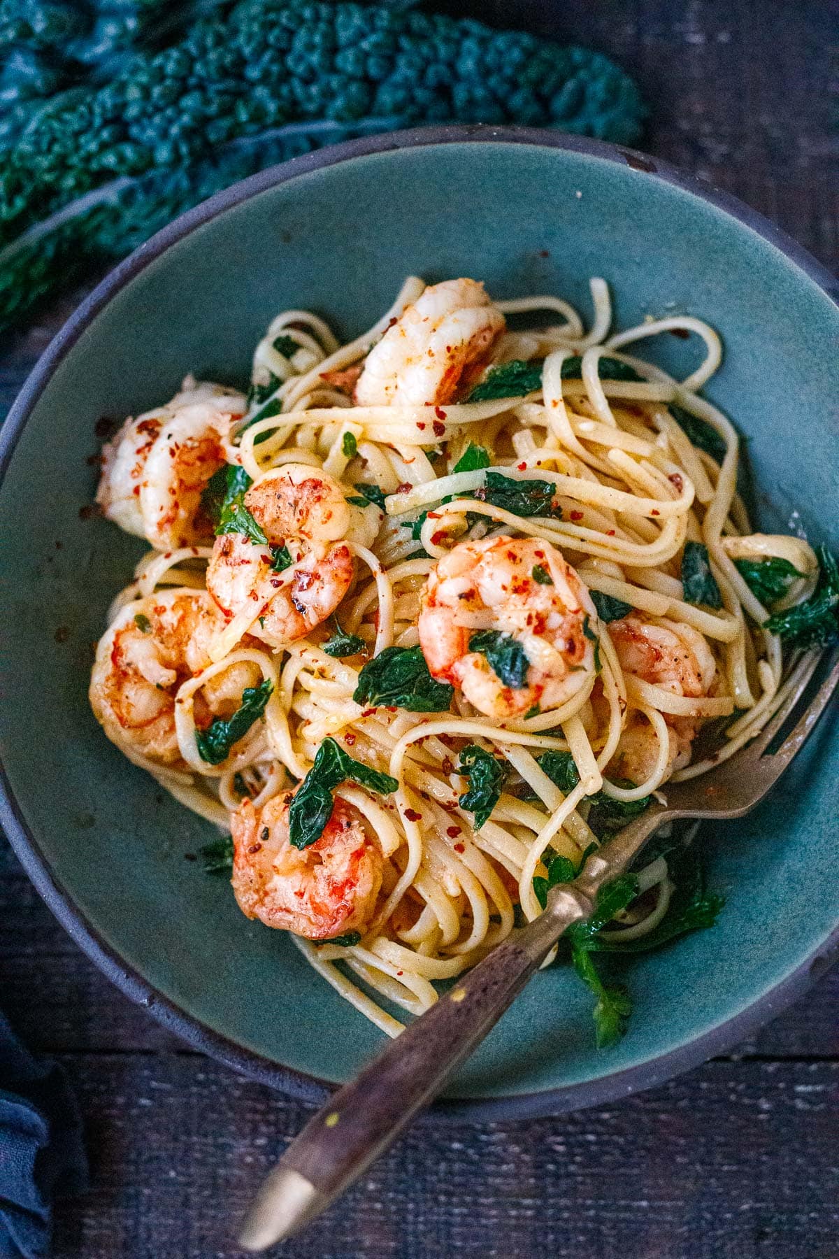 shrimp pasta in blue bowl with wilted kale and red pepper flakes