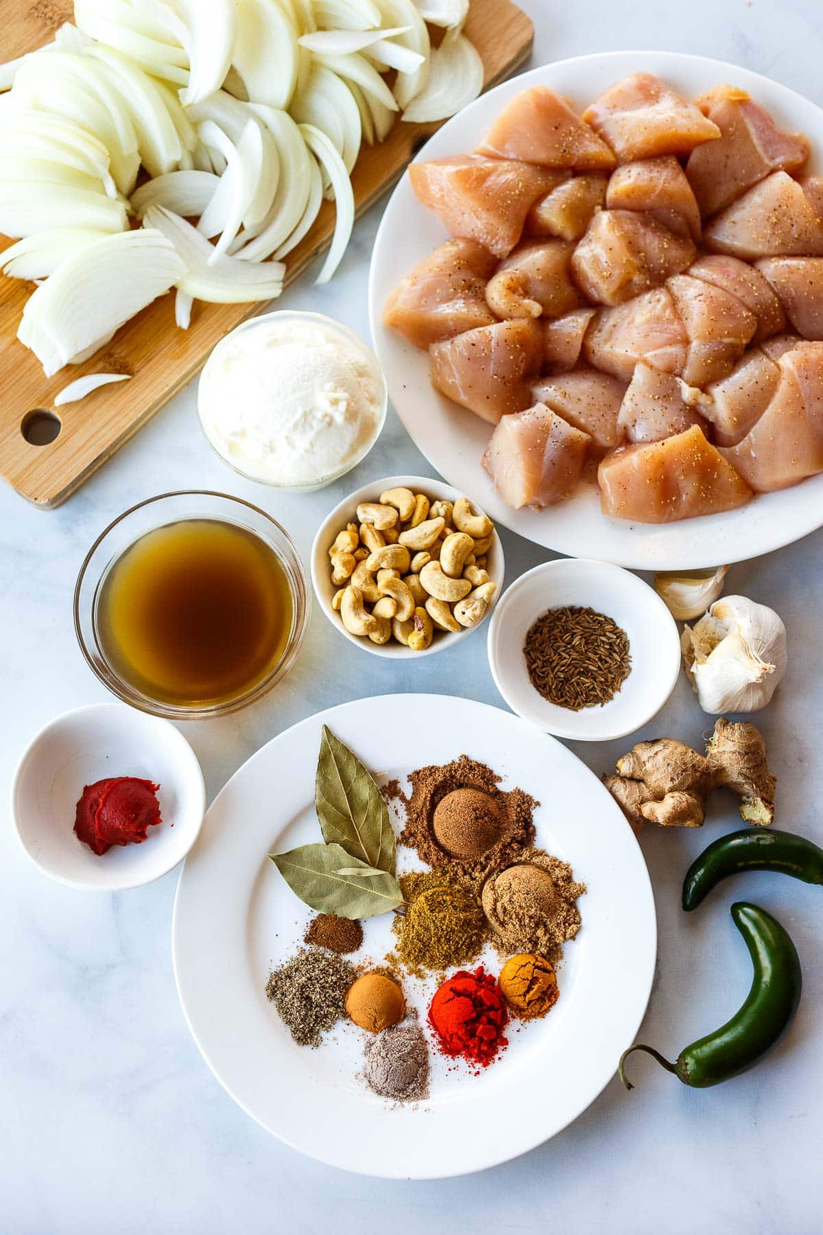 ingredients for chicken korma on counter - boneless chicken, sliced onions, cashews, spices, ginger, garlic, serranos