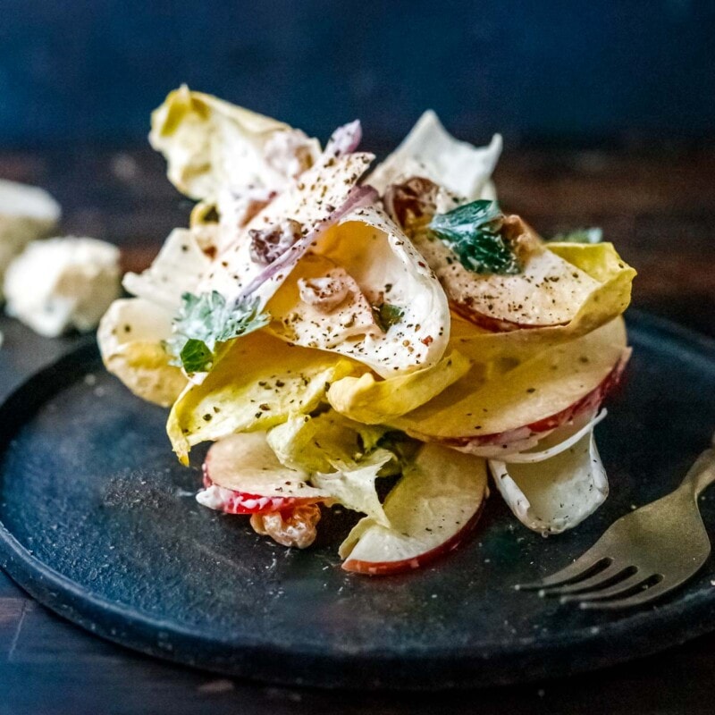 endive salad stacked on plate with homemade blue cheese dressing, sliced apples, red onion, walnuts
