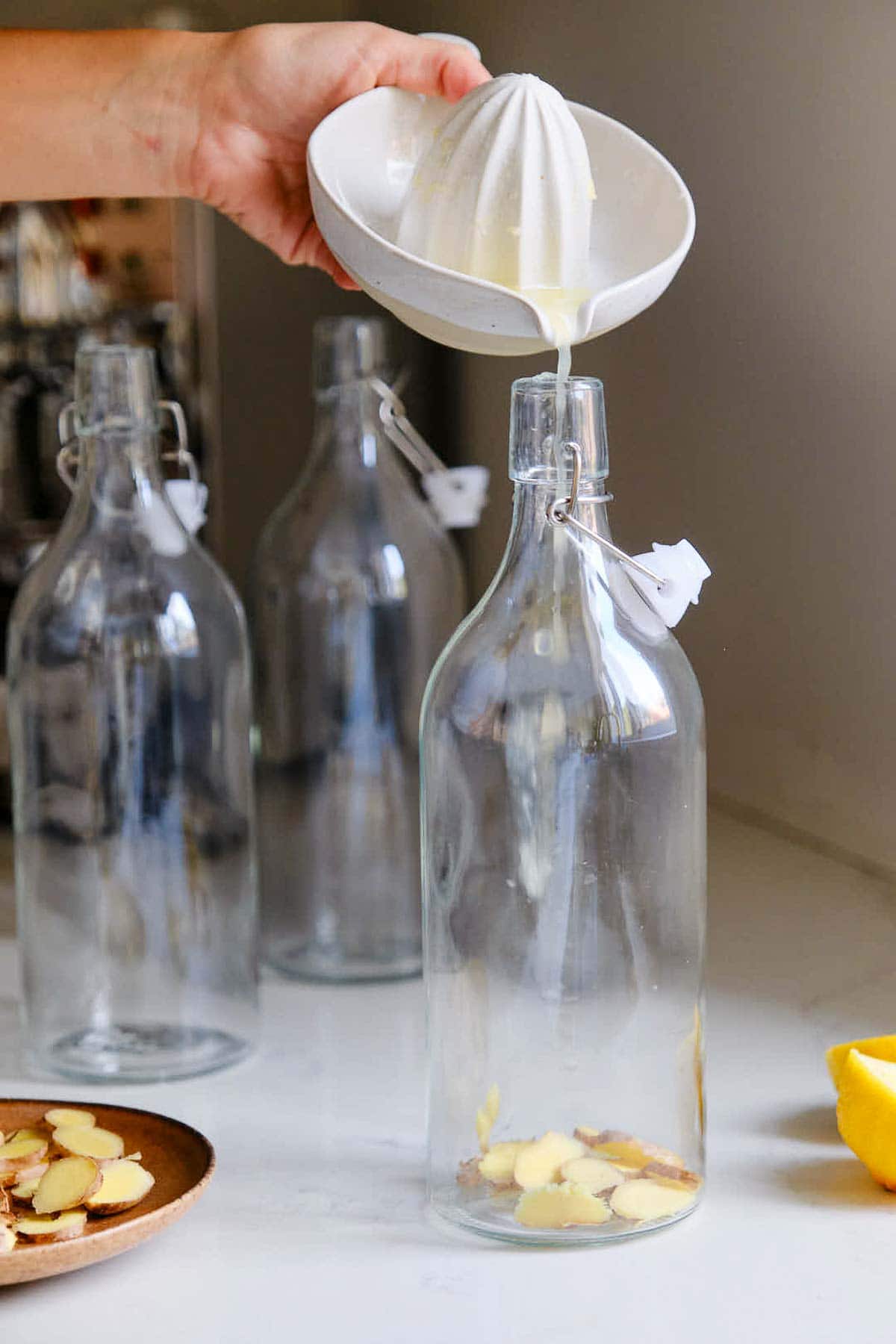 hand pouring lemon juice into glass bottle with sliced ginger.
