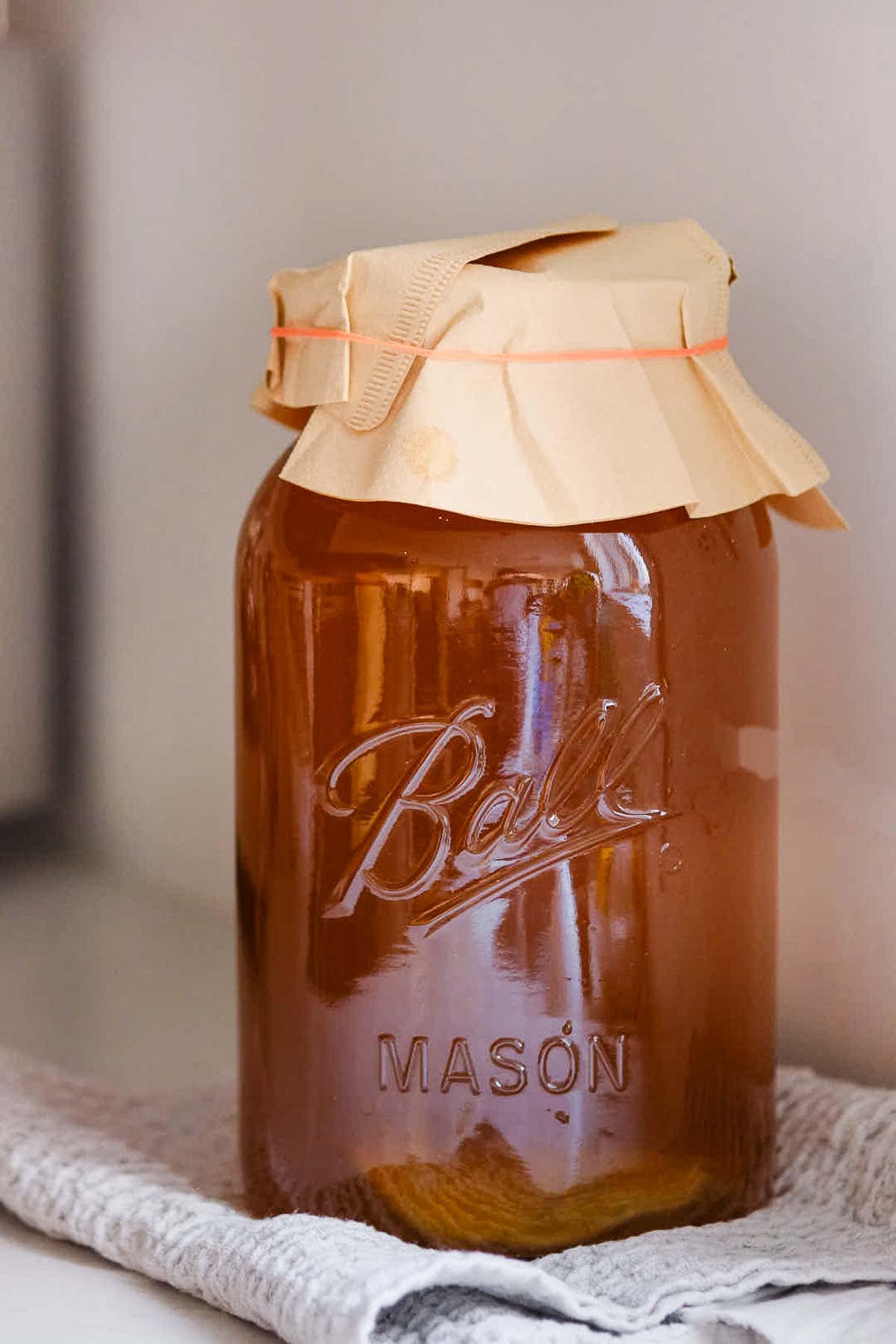 large mason jar of tea with scoby covered with coffee filter and rubber band to ferment.