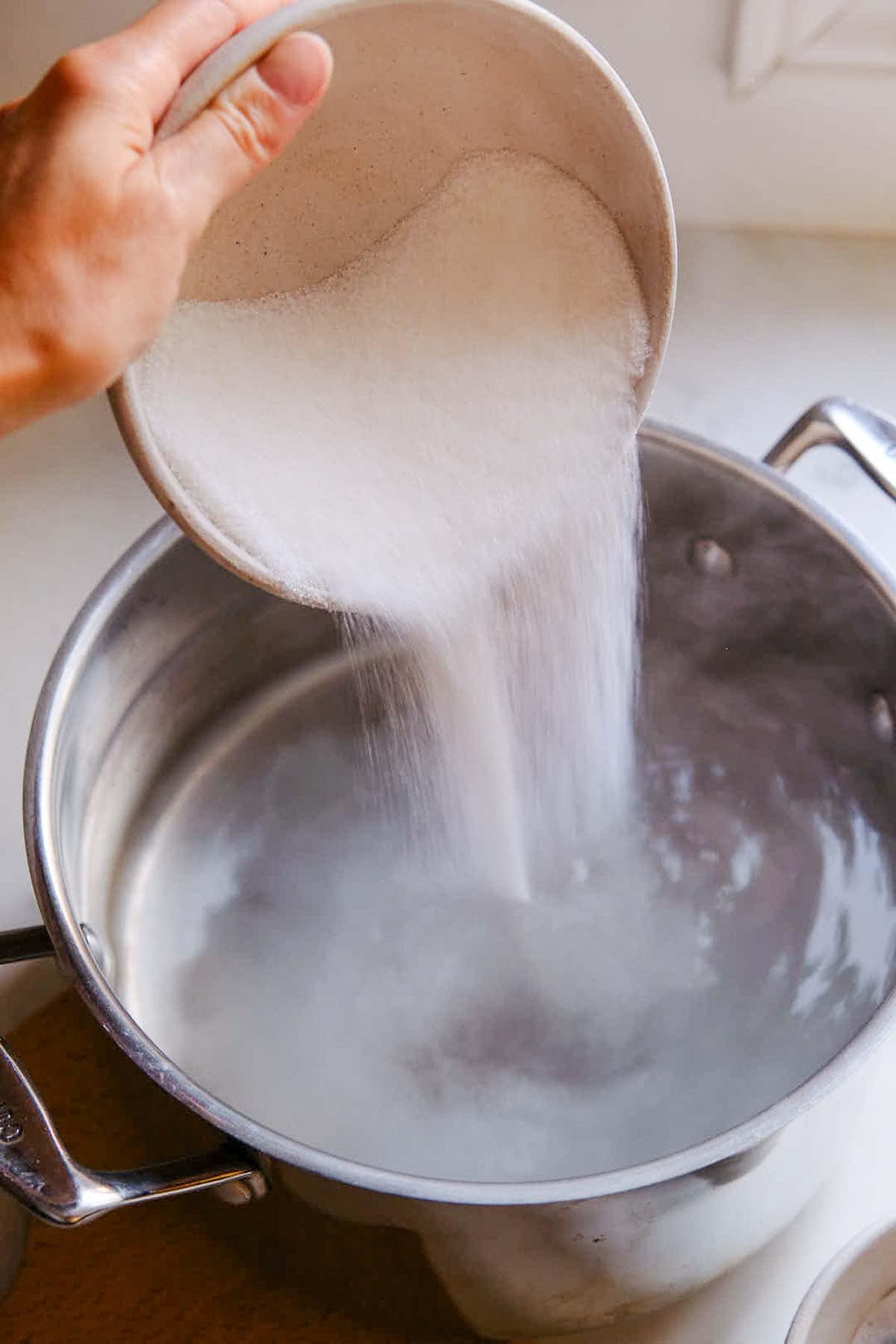 pouring bowl of sugar into large pot of hot water.
