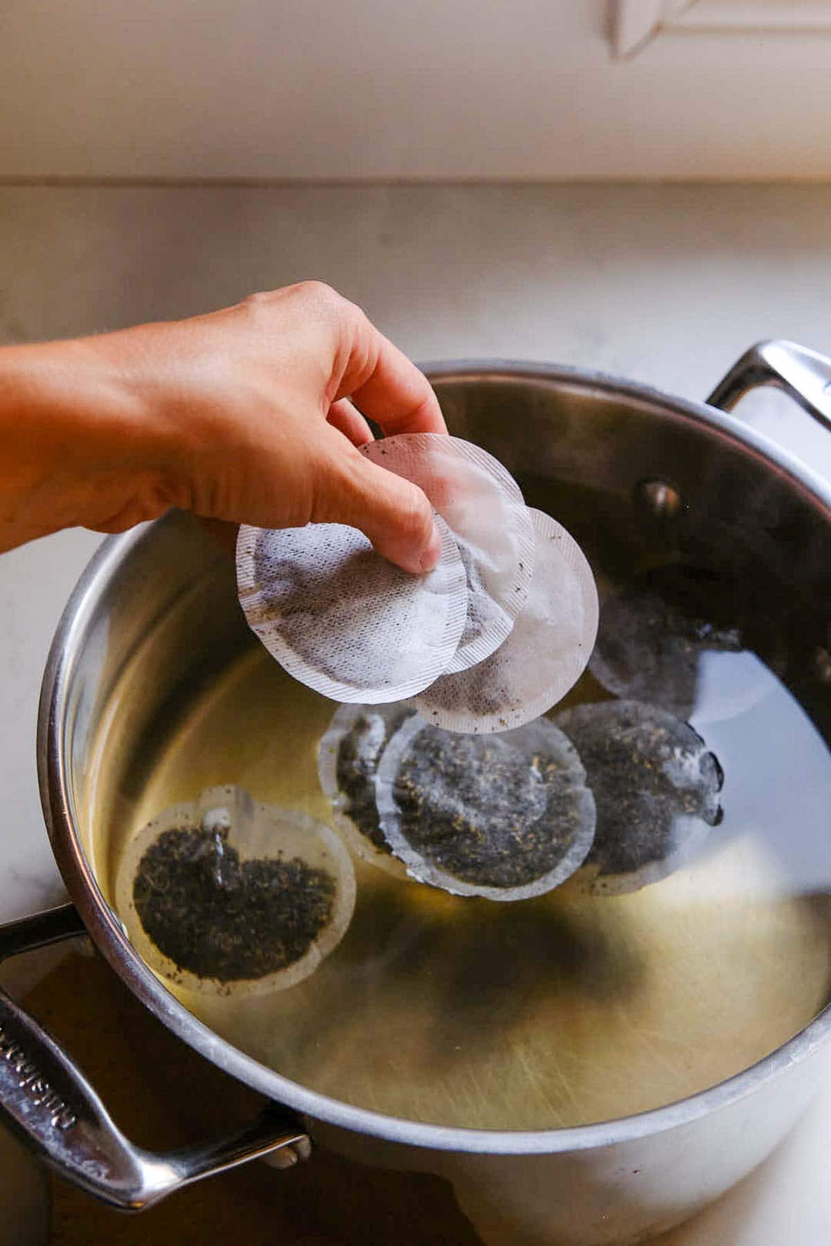 dropping tea bags into large pot of sugar water.