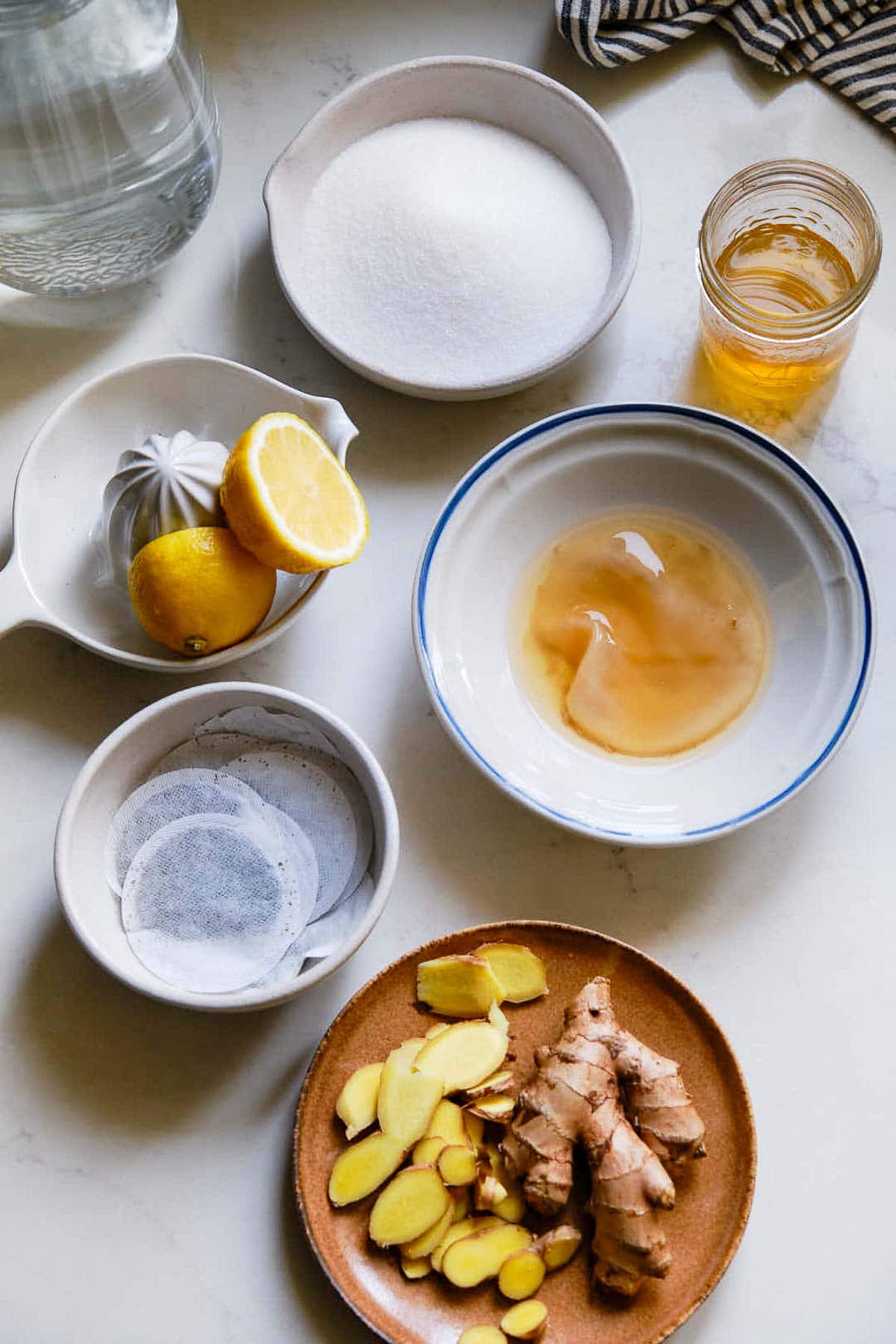 ingredients for kombucha laid out - sugar, kombucha, scoby, lemon halves, tea bags, sliced ginger.